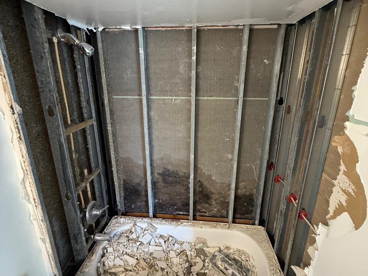 Bathroom stripped to the studs with water damage behind the tub