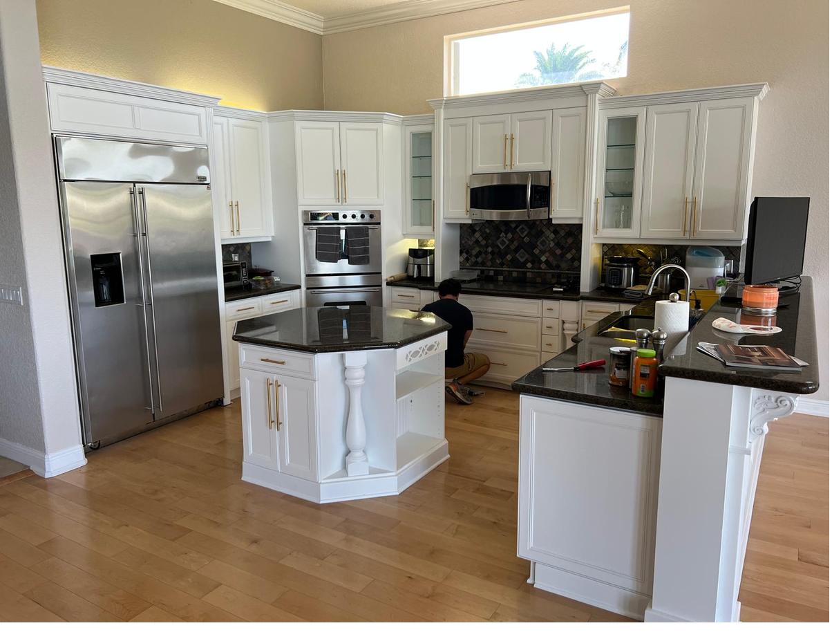Same kitchen after refinishing, with bright white cabinets and gold hardware