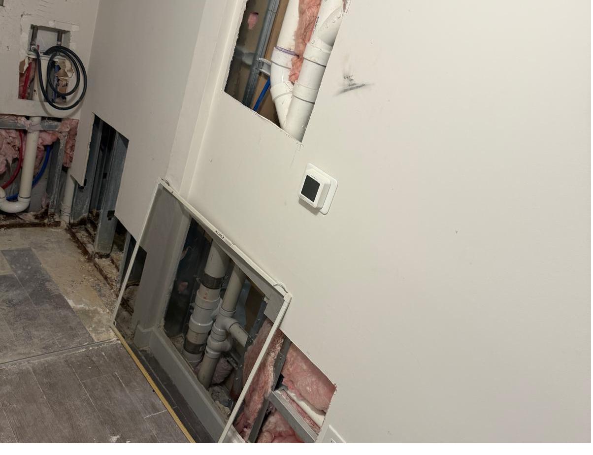 Wall with open drywall cutouts exposing pipes after plumbing work